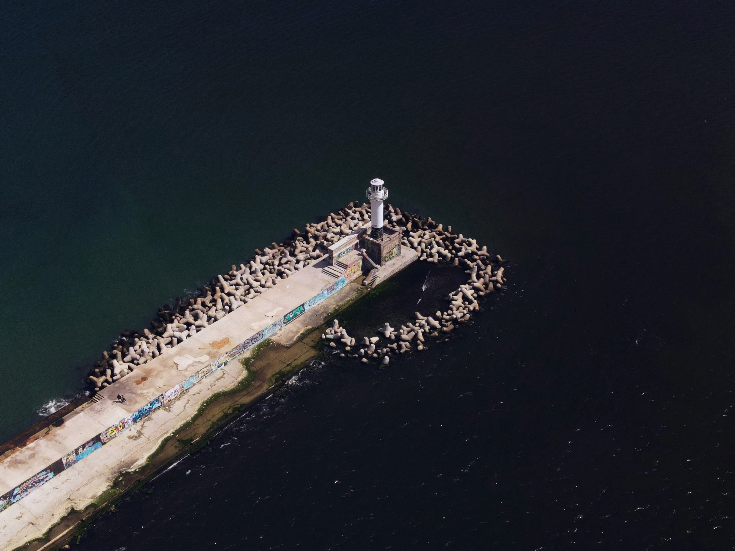 The white lighthouse at the end of the Varna breakwater, seen from above over the dark sea