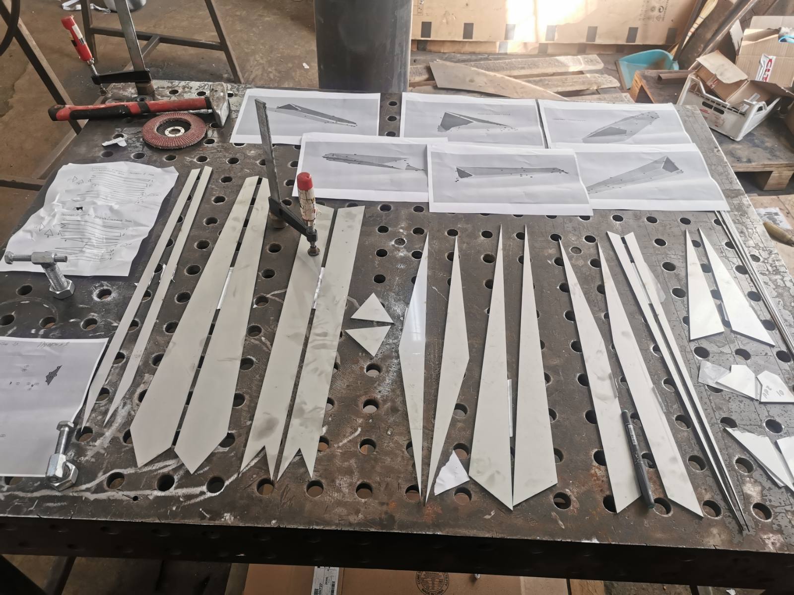 Laser-cut stainless-steel parts laid out beside printed assembly drawings