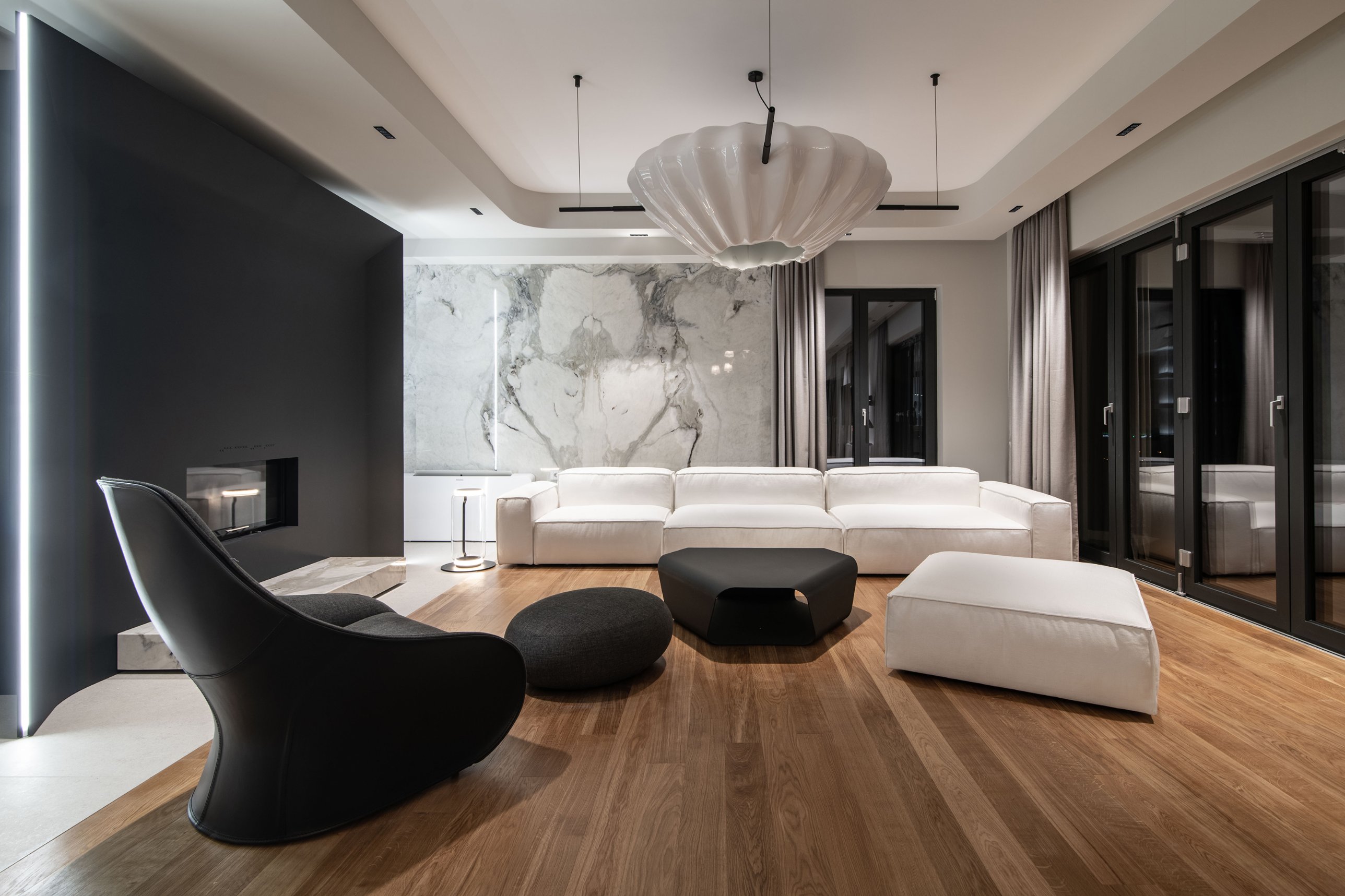 Living room with a black steel fireplace, a white coral-like chandelier and marble-clad walls