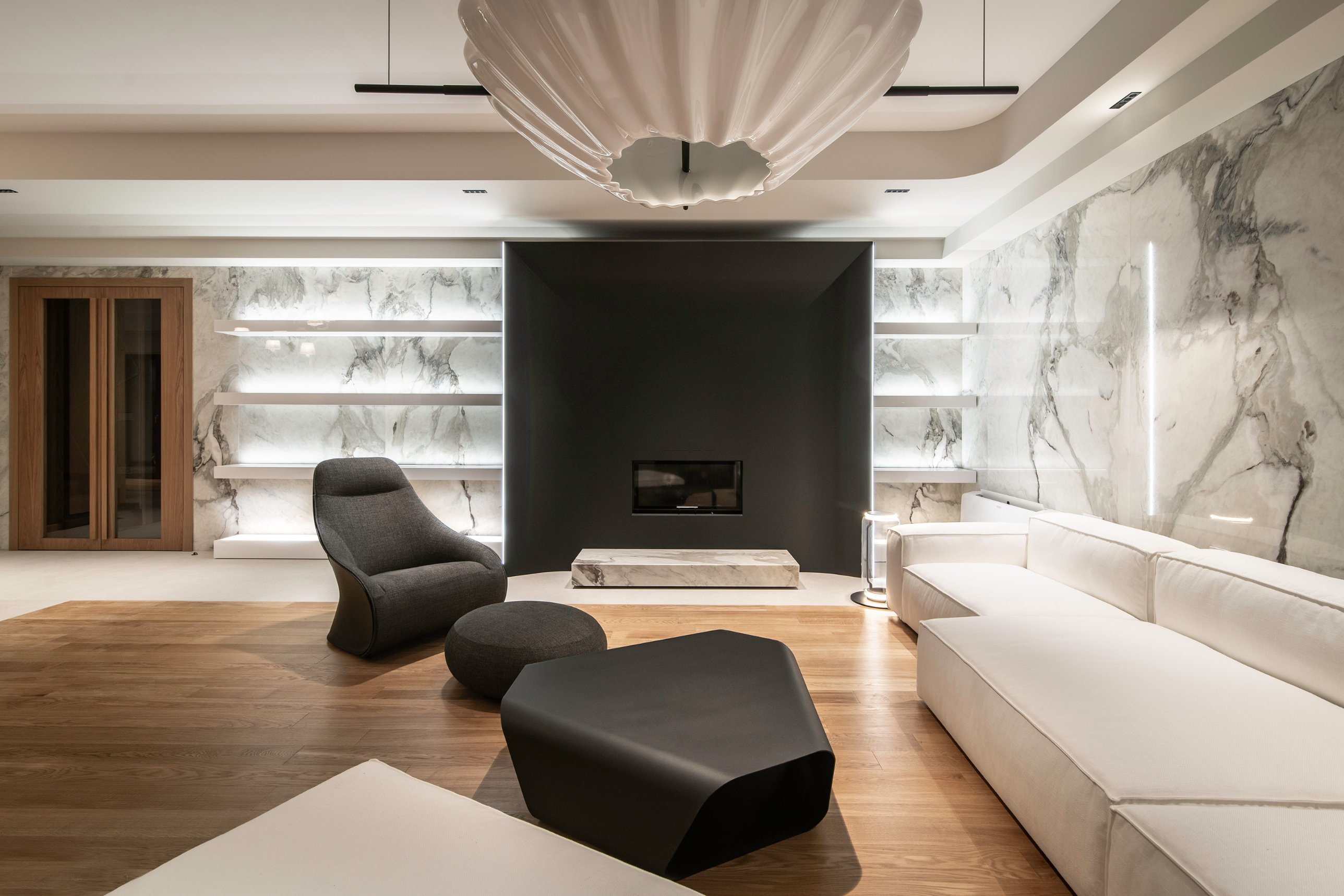 The black steel fireplace between illuminated marble shelves, beneath the coral chandelier